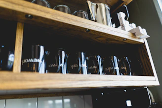 Elegant ceramic mugs and coffee accessories arranged on a rustic wooden shelf.