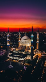 An elegant mosque exterior at sunset, with golden light highlighting intricate Islamic patterns and green accents.