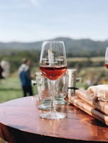Elegant bottles of red and white wine arranged on a rustic wooden table with vineyard hills in the background.