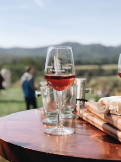 Elegant bottles of red and white wine arranged on a rustic wooden table with vineyard hills in the background.