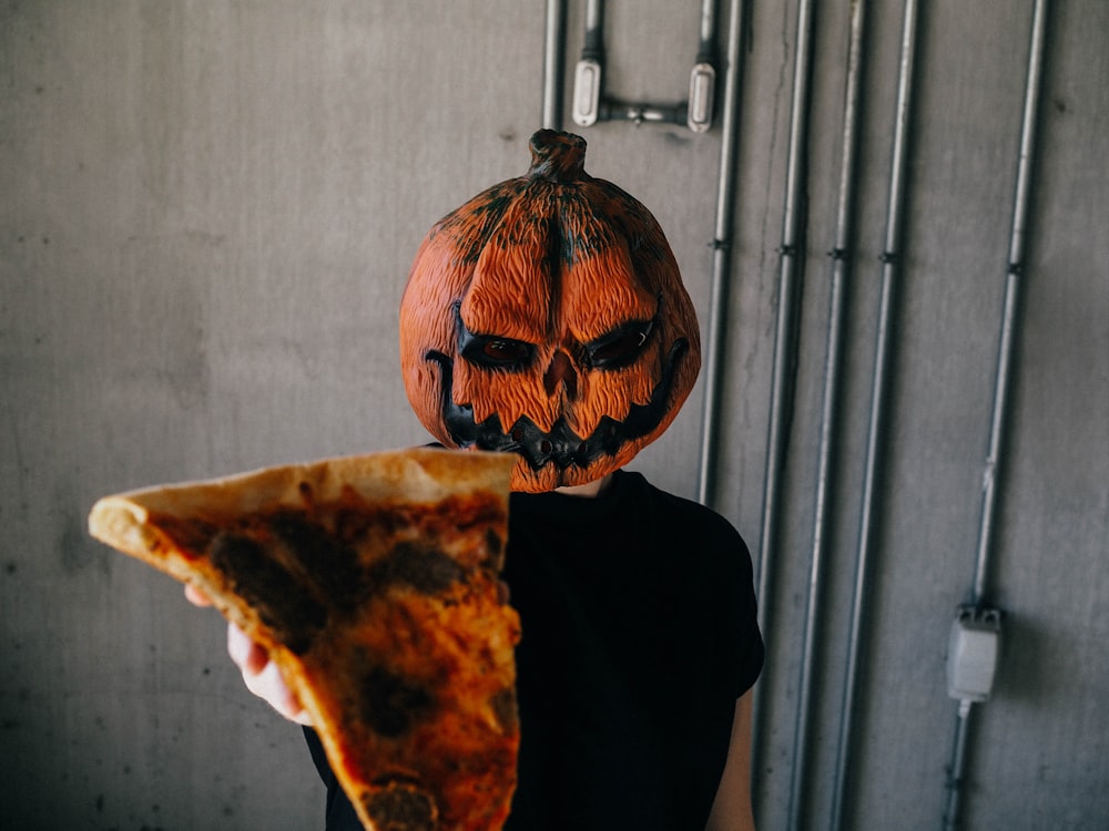 man wearing Jack'-o-lantern mask holding sliced pizza
