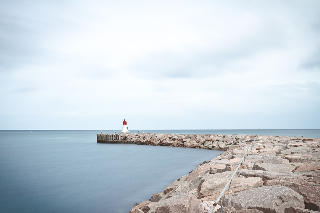 white and red lighthouse near sea at daytime