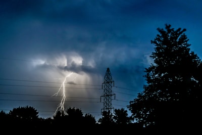 silhouette photo of trees near electric tower under lightning