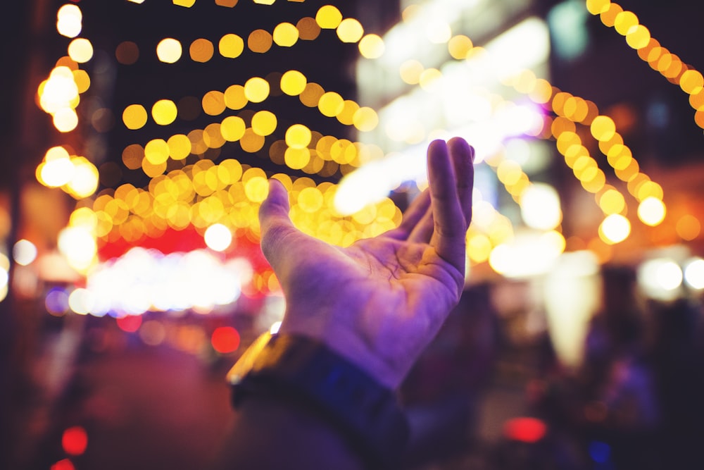 selective focus photography of person's left hand with yellow bokeh light background