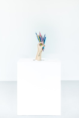 Hand reaching for a pastel-colored pencil from a jar filled with stationery.