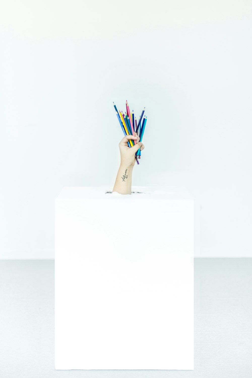 Die Hand einer Person platzte aus der Schachtel mit Stiften in verschiedenen Farben