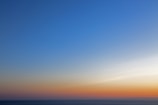 A serene blue sky over a calm ocean horizon at sunrise.