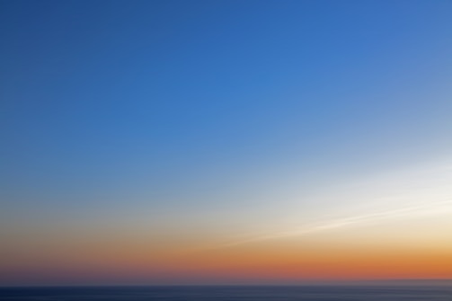 A calm blue ocean horizon meeting a bright sky at sunrise.
