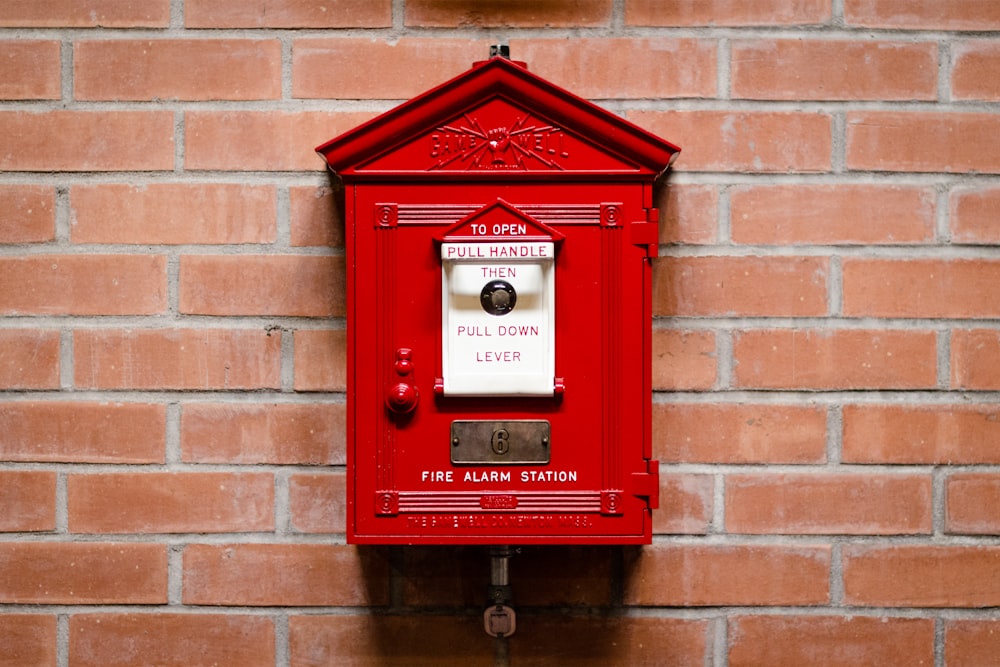 red fire alarm station attached on brick wall