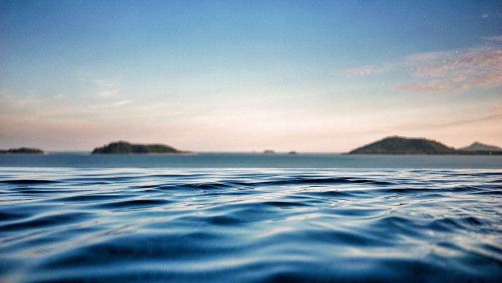 shallow focus photography of ocean with mountain on far side