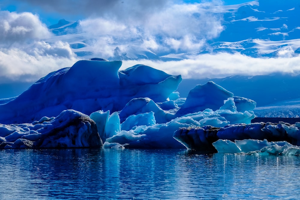 iceberg beside cliff under cloudy sky during daytime