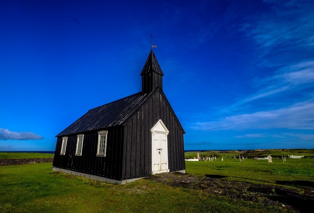 a small black church with a steeple on a grassy field