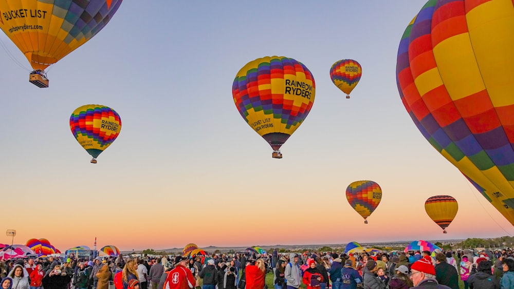 people gathering below multicolored hot air balloons