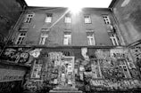 A weathered urban building adorned with various colorful graffiti covers a large portion of the facade. Sunlight beams down from above, creating a dramatic highlight on the structure. The walls are filled with vibrant street art, including tags, characters, and abstract designs, suggesting an expressive urban culture.