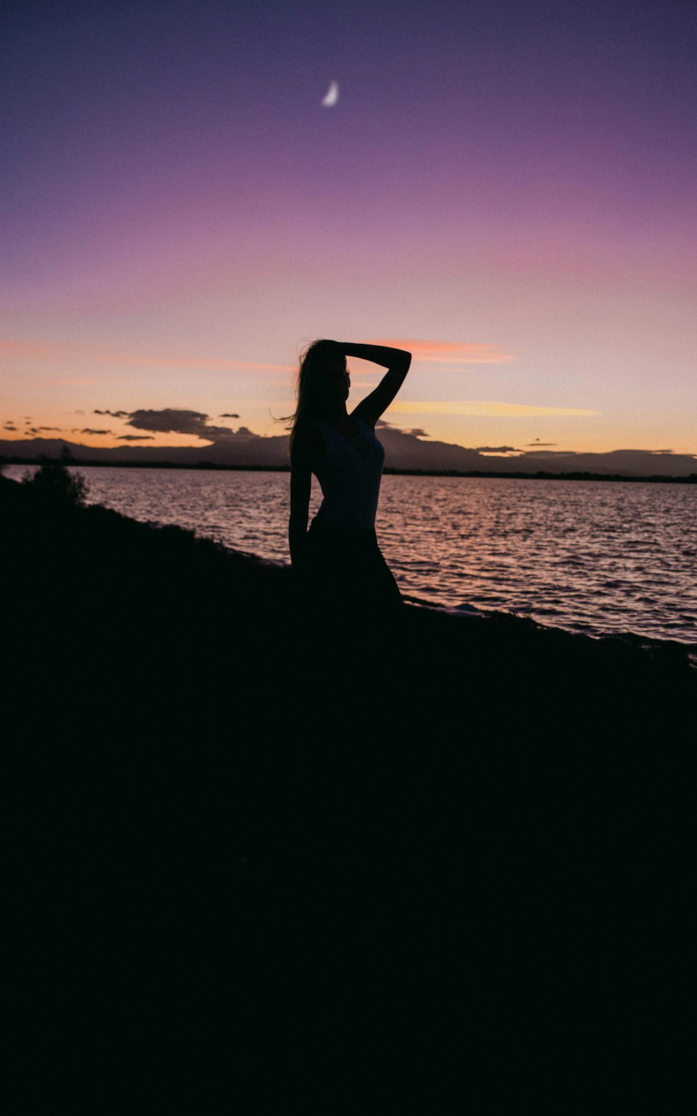 Silhouette einer Frau am Strand mit linker Hand auf dem Kopf