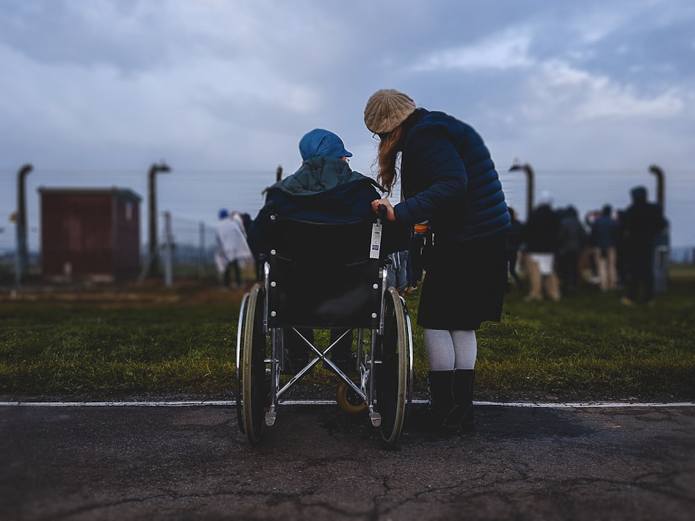 Frau, die in der Nähe einer Person im Rollstuhl in der Nähe eines grünen Grasfeldes steht