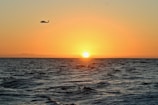 silhouette of helicopter flying above body of water