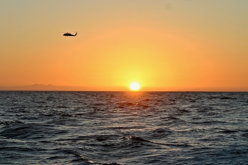 silhouette of helicopter flying above body of water