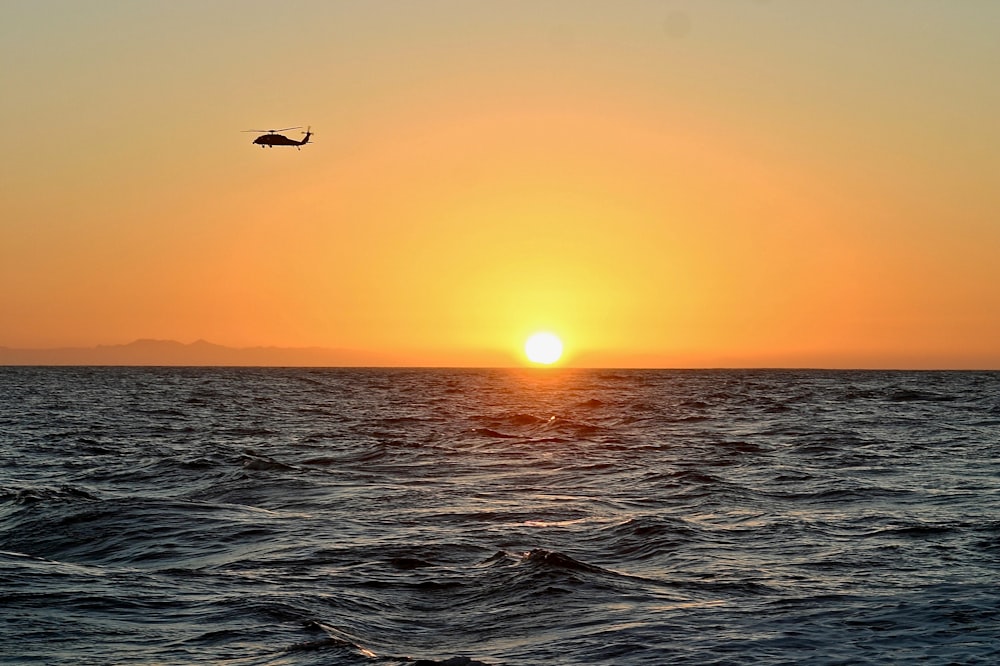 silhouette of helicopter flying above body of water