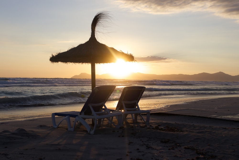 two brown chairs and umbrella on shore during golden hour