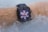 A smartwatch with a floral patterned face submerged in water, worn on a forearm. The water appears bubbly and is splashing around the watch.