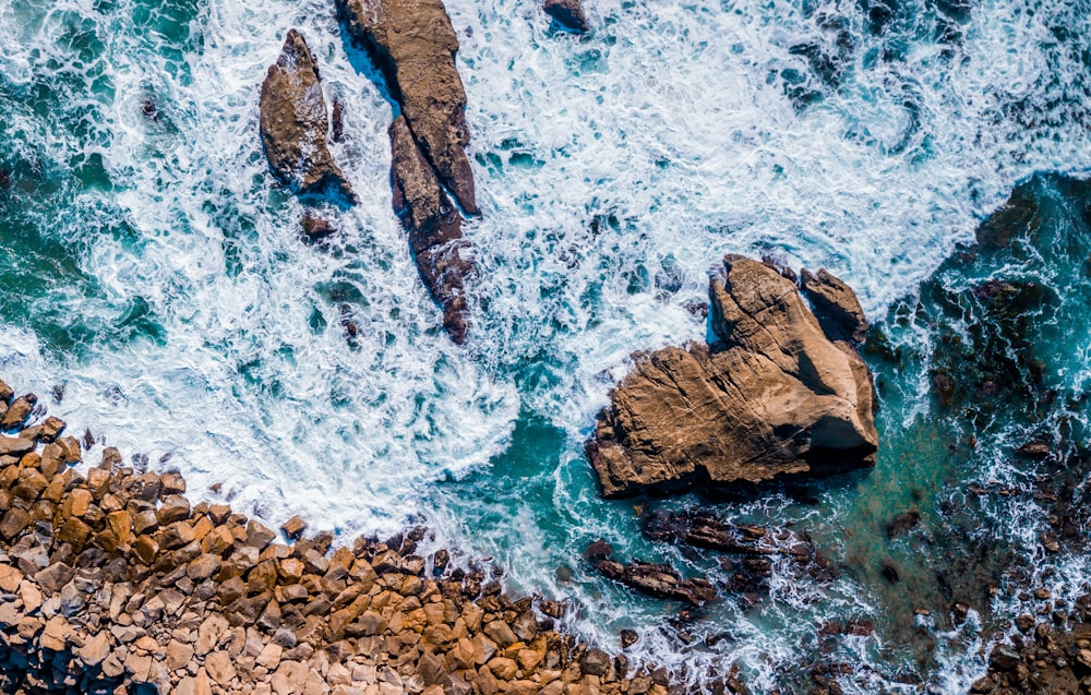 Fotografia a volo d'uccello delle onde del mare che spruzzano sulla roccia durante il giorno
