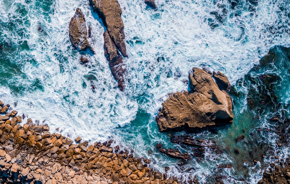 bird's eye view photography of seawaves splashing on rock during daytime