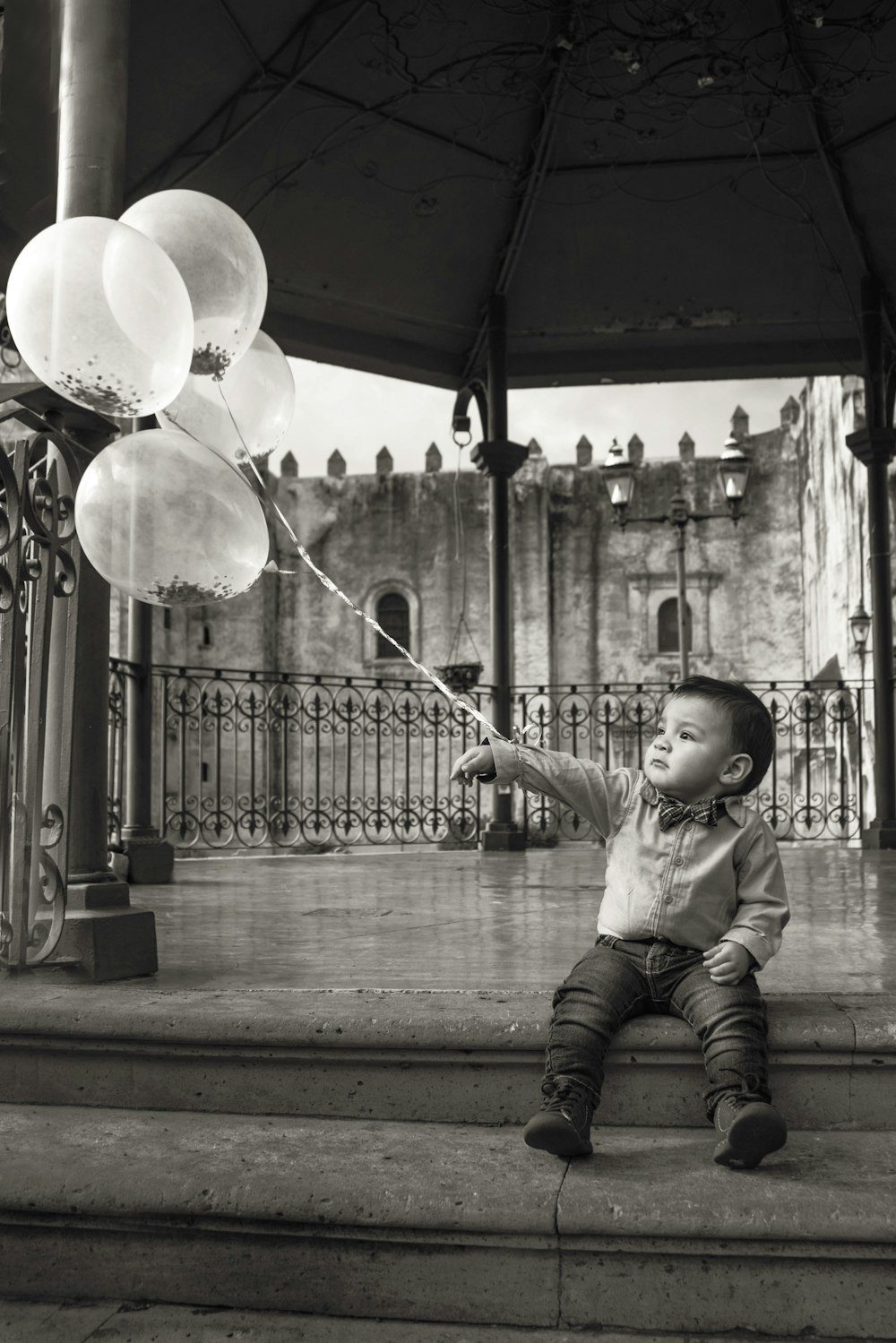 fotografia in scala di grigi di un ragazzo che tiene palloncini