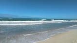 A serene beach with a clear blue sky and gentle waves.