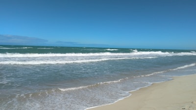 A serene beach view with clear skies and gentle waves lapping at the shore.