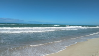 A serene beach view with gentle waves lapping at the shore under a clear blue sky.