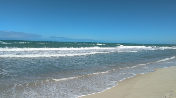 A serene beach view with gentle waves lapping at the shore under a clear blue sky.