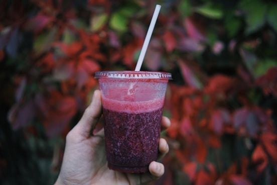 person holding a smoothie glass with a straw in it