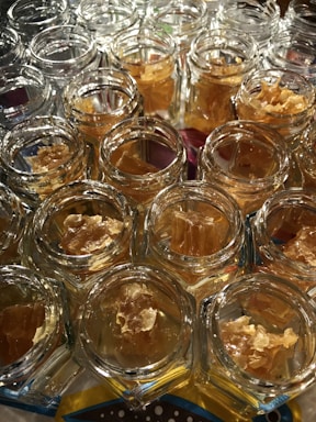 A collection of small glass jars filled with honeycomb. The jars are arranged closely together on a light-reflective surface, emphasizing the hexagonal shapes and golden hues of the honeycomb inside.