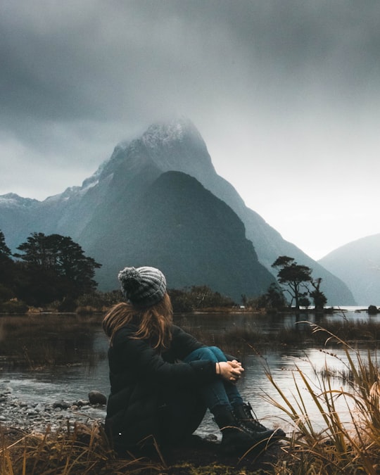 woman sitting near body of water looking at clouds in Milford Sound New Zealand