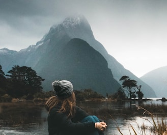 woman sitting near body of water looking at clouds