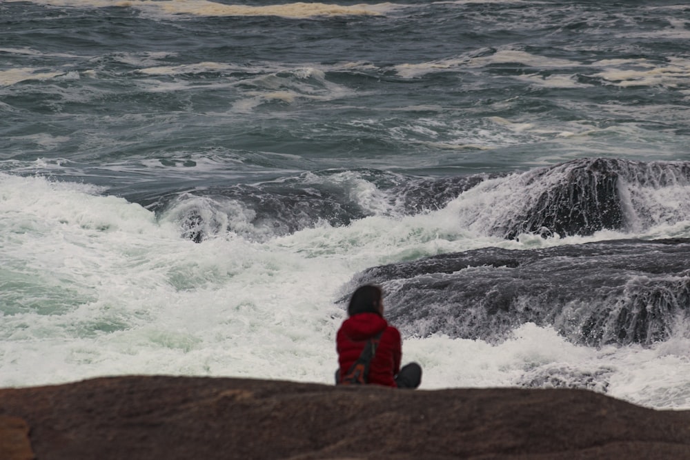 Foto de persona sentada en la roca mirando el mar