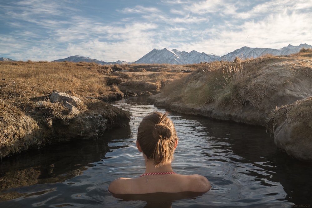 woman immerged in body of water between lands under cloudy sky