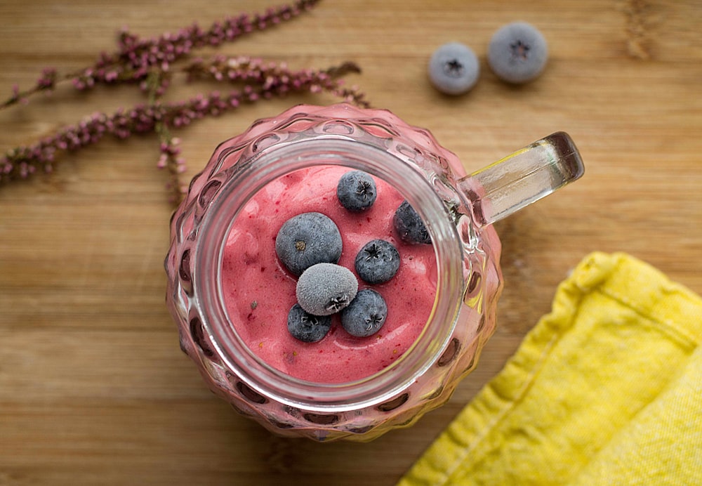 분홍색 액체와 블루베리로 채워진 투명 컷 유리 머그잔