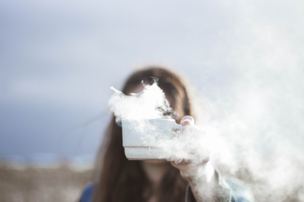 person holding white ceramic cup with smoke flowing inside