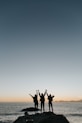 silhouette photography of persons raising hands while standing on island