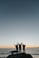 silhouette photography of persons raising hands while standing on island