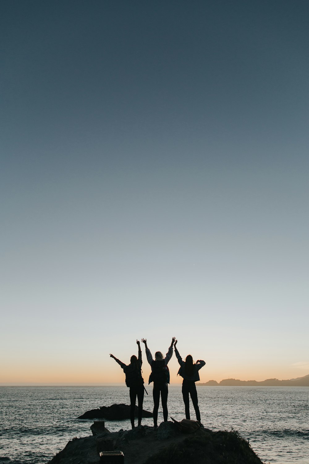 silhouette photography of persons raising hands while standing on island