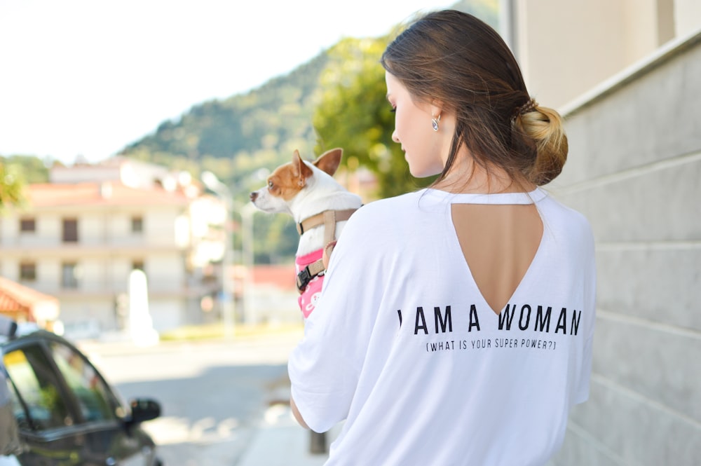 woman wearing white elbow-sleeved shirt while holding dog near concrete building during daytime