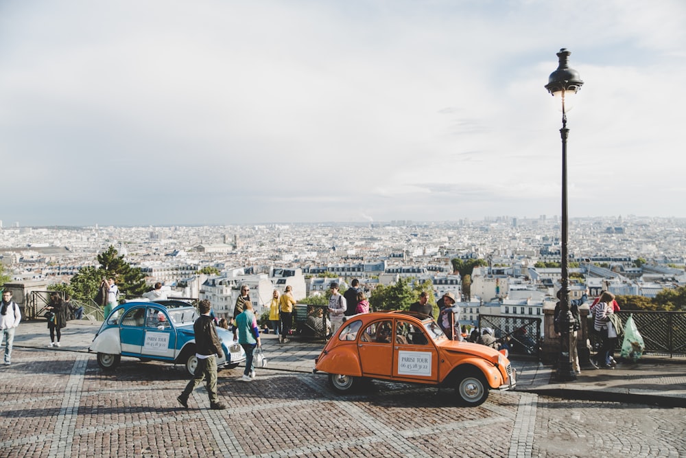 two cars parked beside a road with people walking by