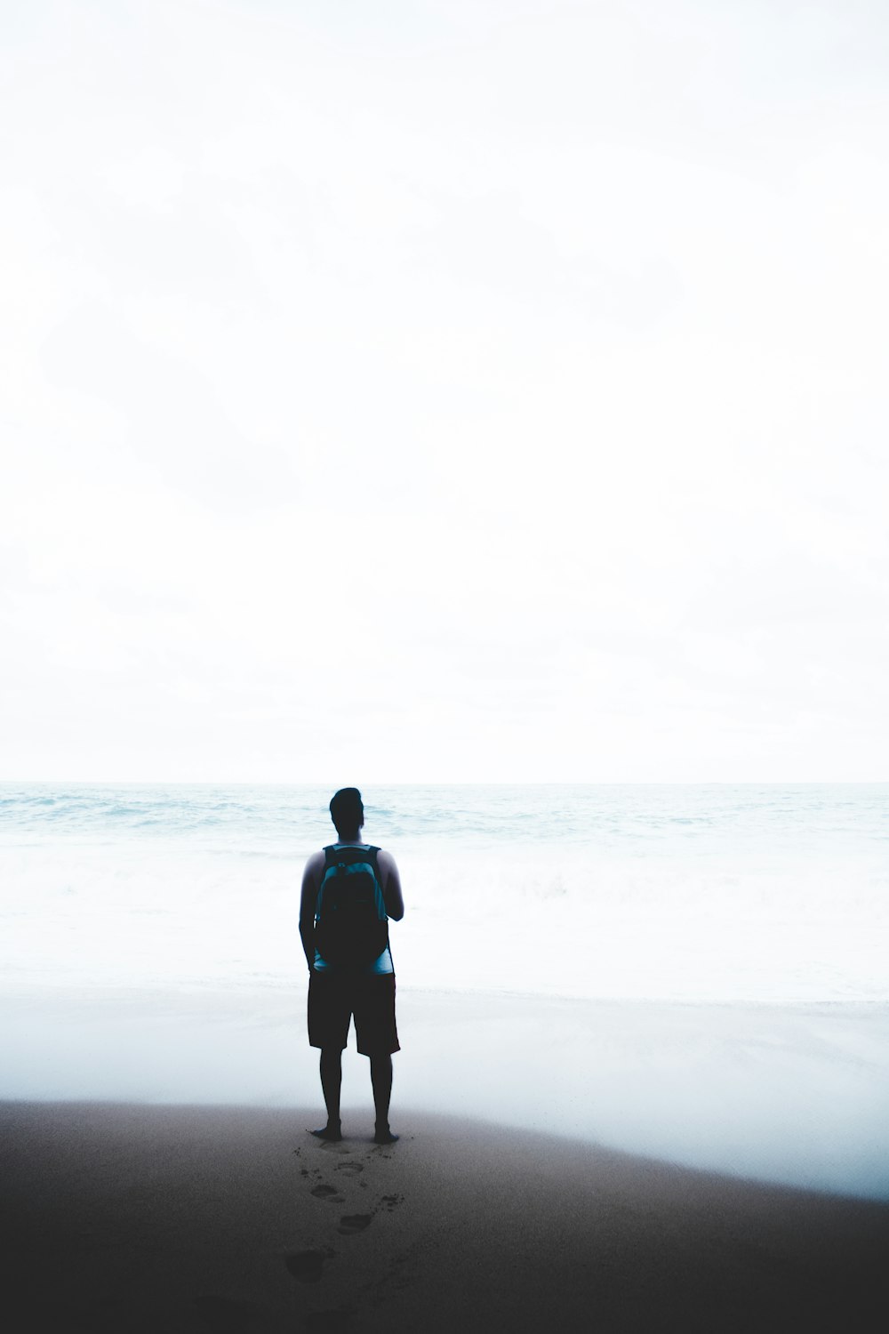 man standing in front of body of water while carrying blue and black backpack