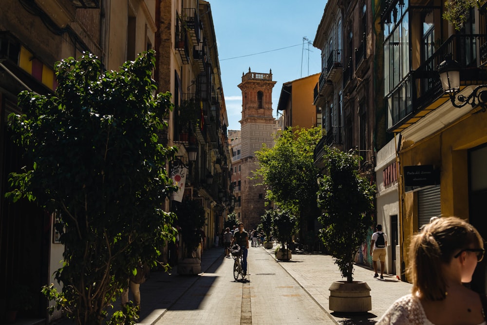 man riding bicycle near narrow street surrounded by buildings during daytime