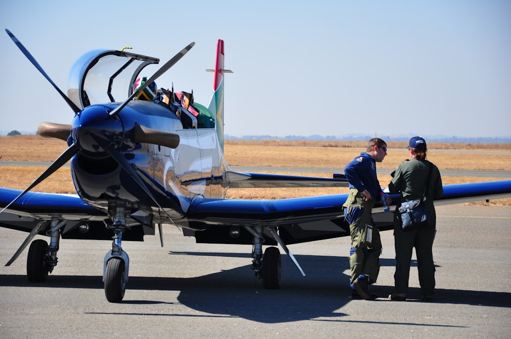 two persons standing near blue jet plane during daytime