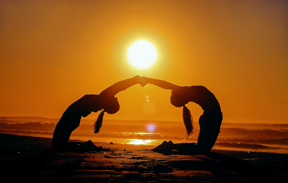 Silueta de dos mujeres que se doblan mientras se toman de la mano durante la puesta del sol