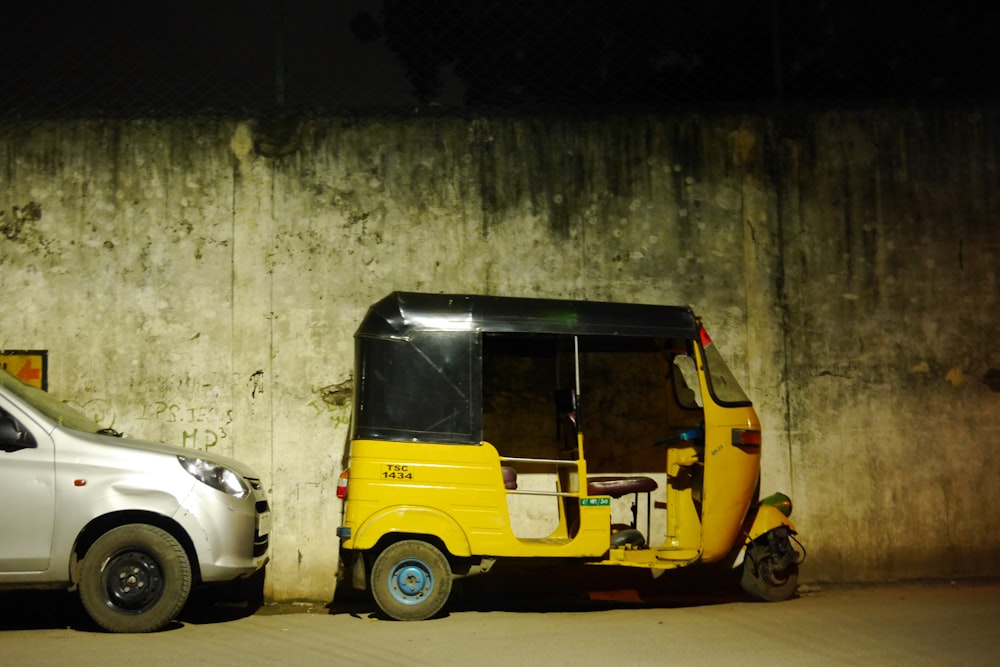 Auto rickshaw al lado de un muro de hormigón y un coche plateado